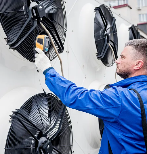 Technician in blue uniform using a handheld device to check the temperature of large industrial ventilation fans.