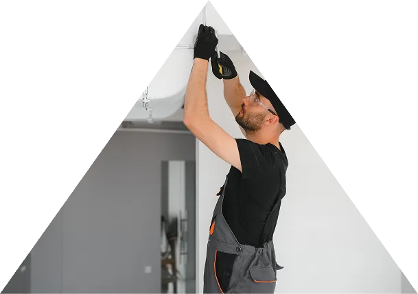 Worker wearing gloves and safety goggles uses a screwdriver to fix a light fixture on a ceiling indoors.