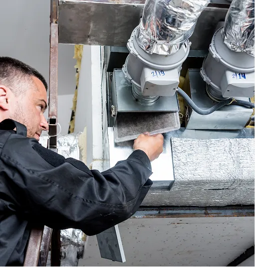 Technician wearing a black uniform inspecting a HVAC air filter inside a ventilation system.