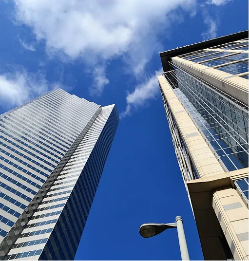 Low-angle view of two modern skyscrapers against a bright blue sky with scattered clouds and a street lamp in the foreground.