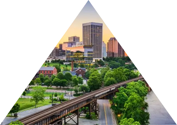 City skyline at sunset with train tracks and green trees along a river.