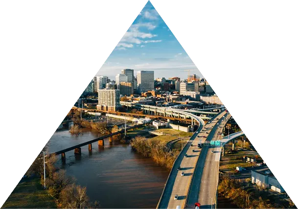 Aerial view of a highway and river with a city skyline under a partly cloudy sky.