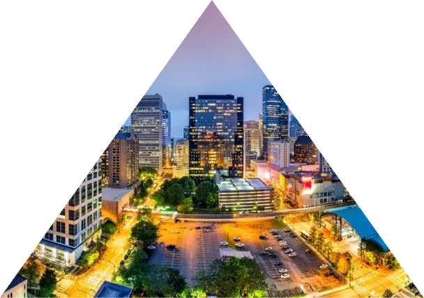 Evening cityscape with illuminated buildings and streets viewed through a triangular frame.