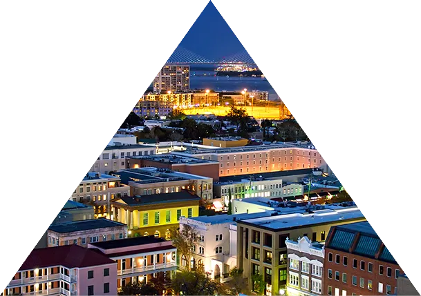 Nighttime cityscape with illuminated buildings and a bridge over water in the background, framed within a triangular shape.