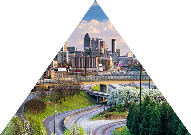 Curved highways surrounded by green trees leading towards a city skyline under a partly cloudy sky.