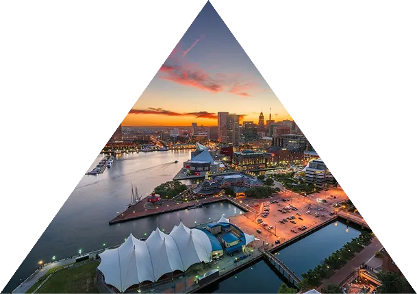 Aerial view of Baltimore Inner Harbor at sunset with water, city skyline, and illuminated buildings.