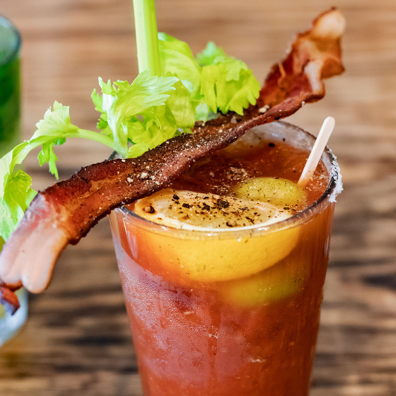 A vibrant Bloody Mary garnished with crisp celery, a lemon wedge, and crispy bacon. 