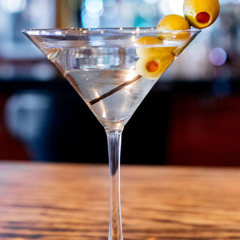A classic martini in a clear glass with three green olives on a skewer.