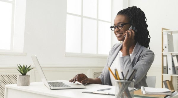 Woman talking on the phone while typing on her laptop.