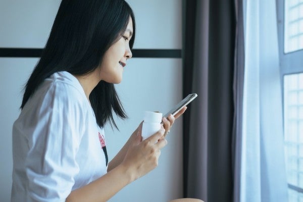 Woman looking at her phone while holding a pill bottle.