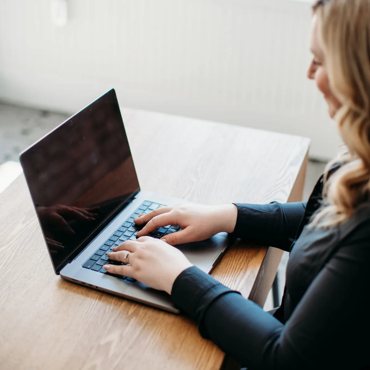 Woman typing on a laptop with a wooden table background.