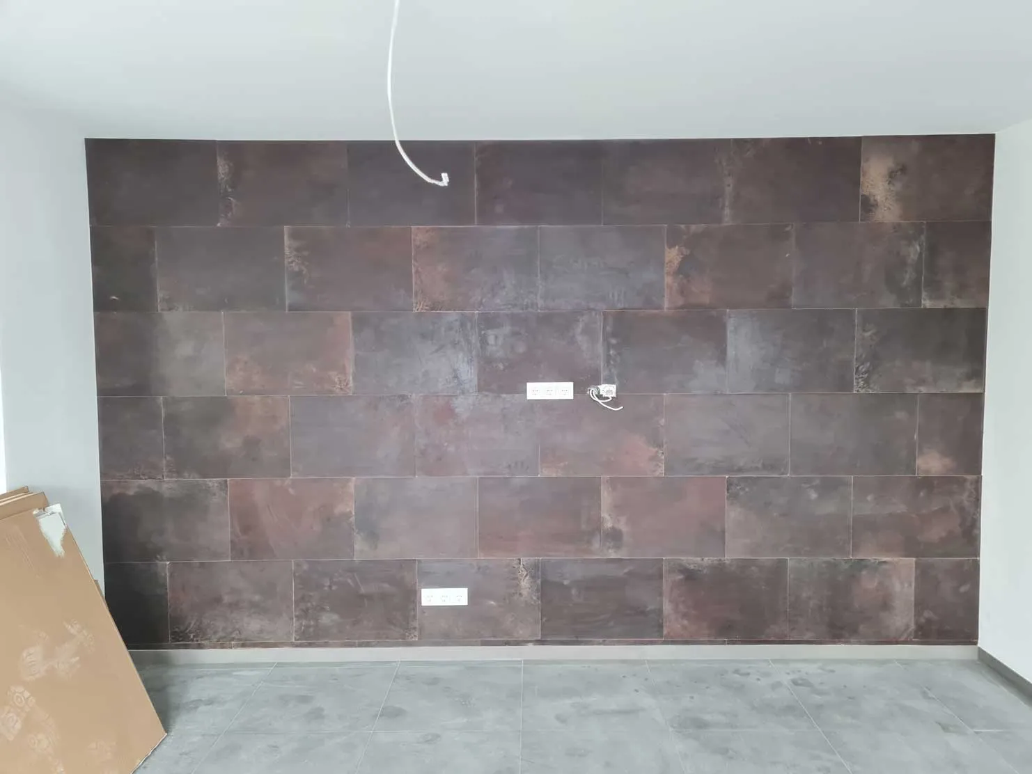 Innere Wand mit braunen rechteckigen Fliesen und mehreren Steckdosen, grauer Boden und weiße Decke.
