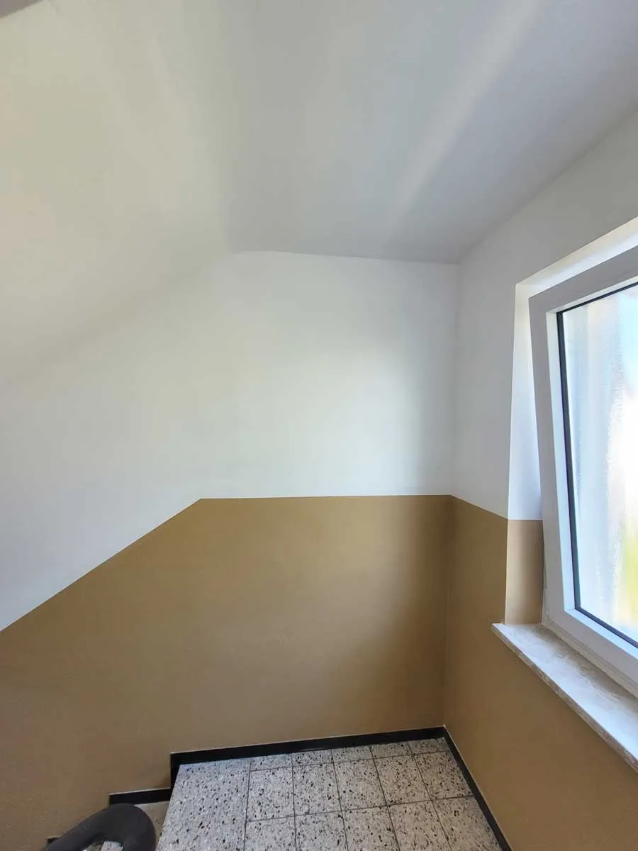 Treppenhaus mit beige-weiß gestrichener Wand und einem Fenster mit Milchglas.