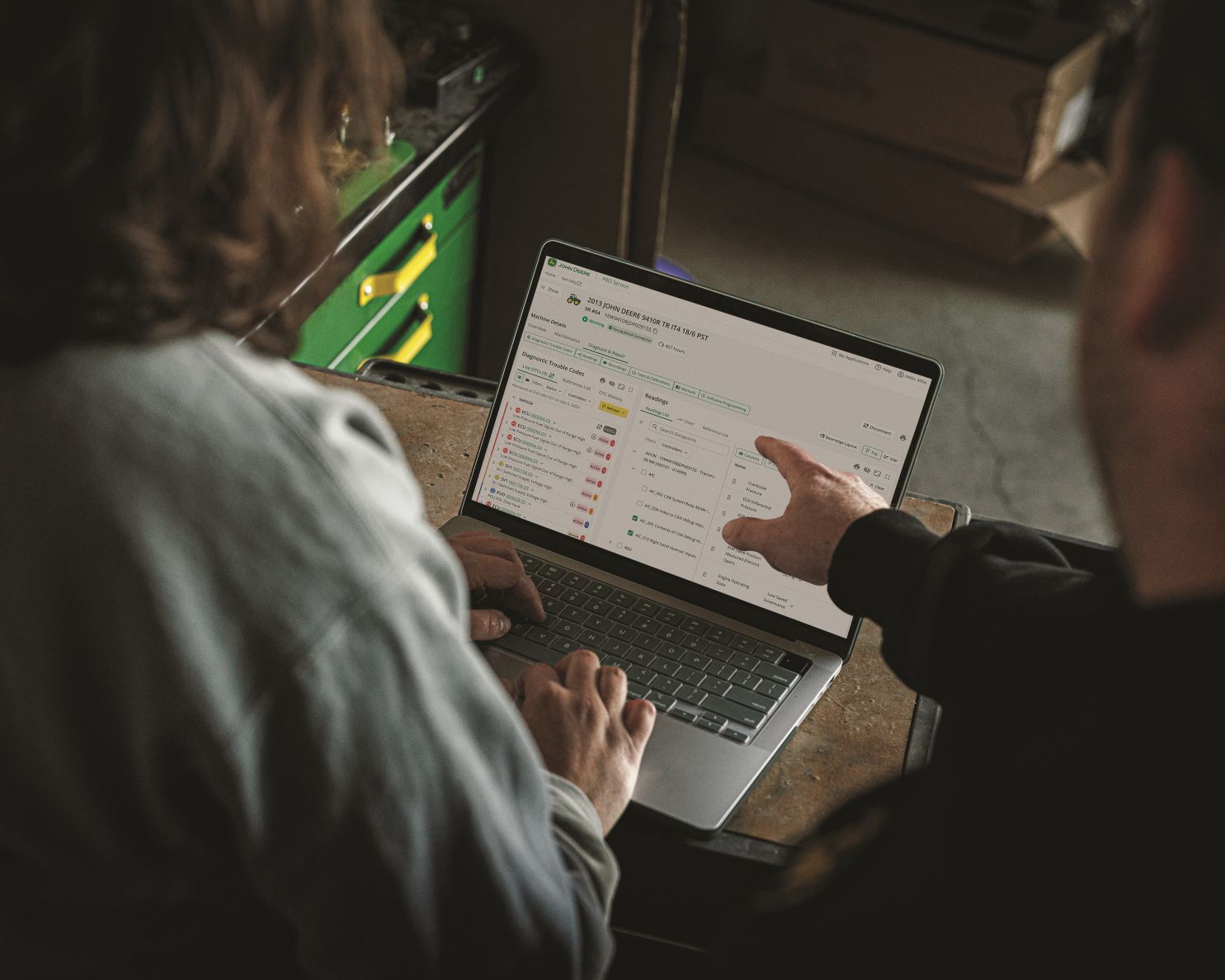 Two people looking at a laptop screen displaying diagnostic trouble codes for a John Deere machine.
