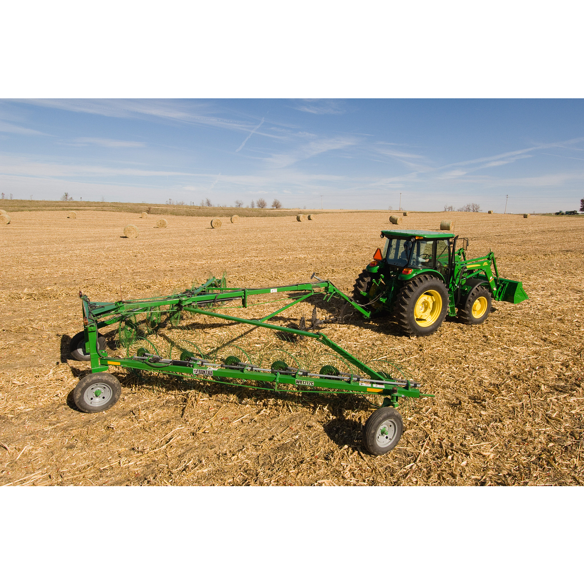 Side right view of a green John Deere tractor pulling a WR1212 High-Capacity Wheel Rake across a harvested field
