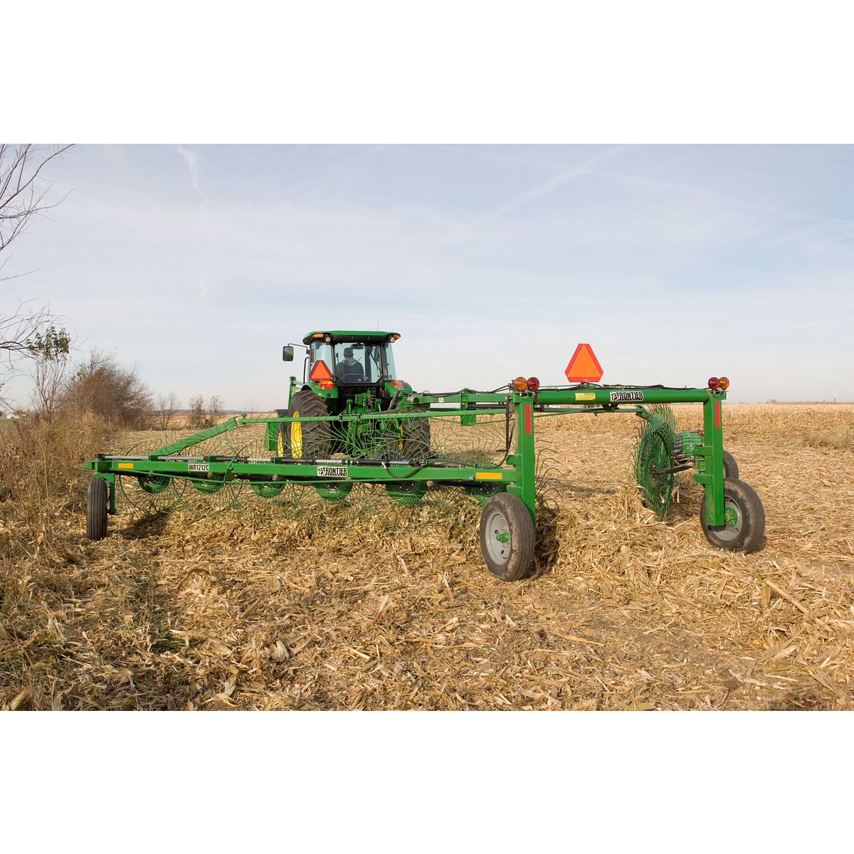 Rear view of a WR1212 High-Capacity Wheel Rake being pulled across a harvested field by a tractor