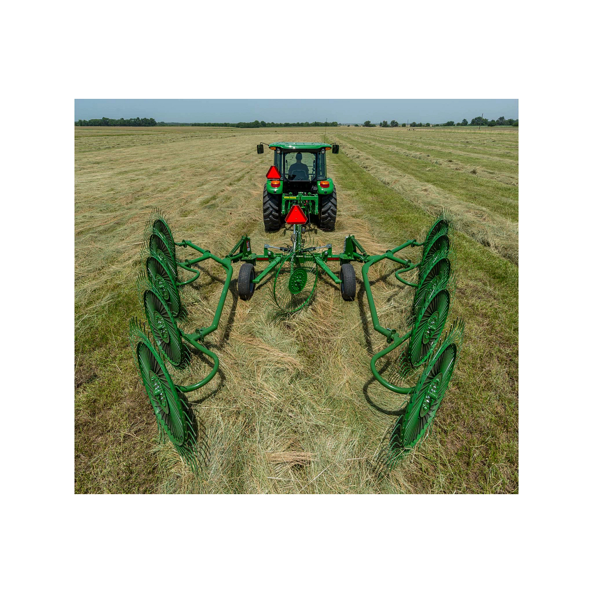 Rear view of a tractor pulling a WR00 wheel rake across a hay field