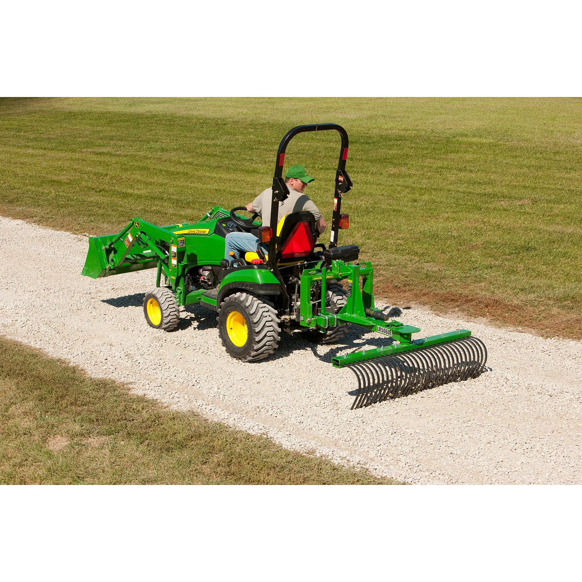 Man drives tractor pulling a landscape rake on a road