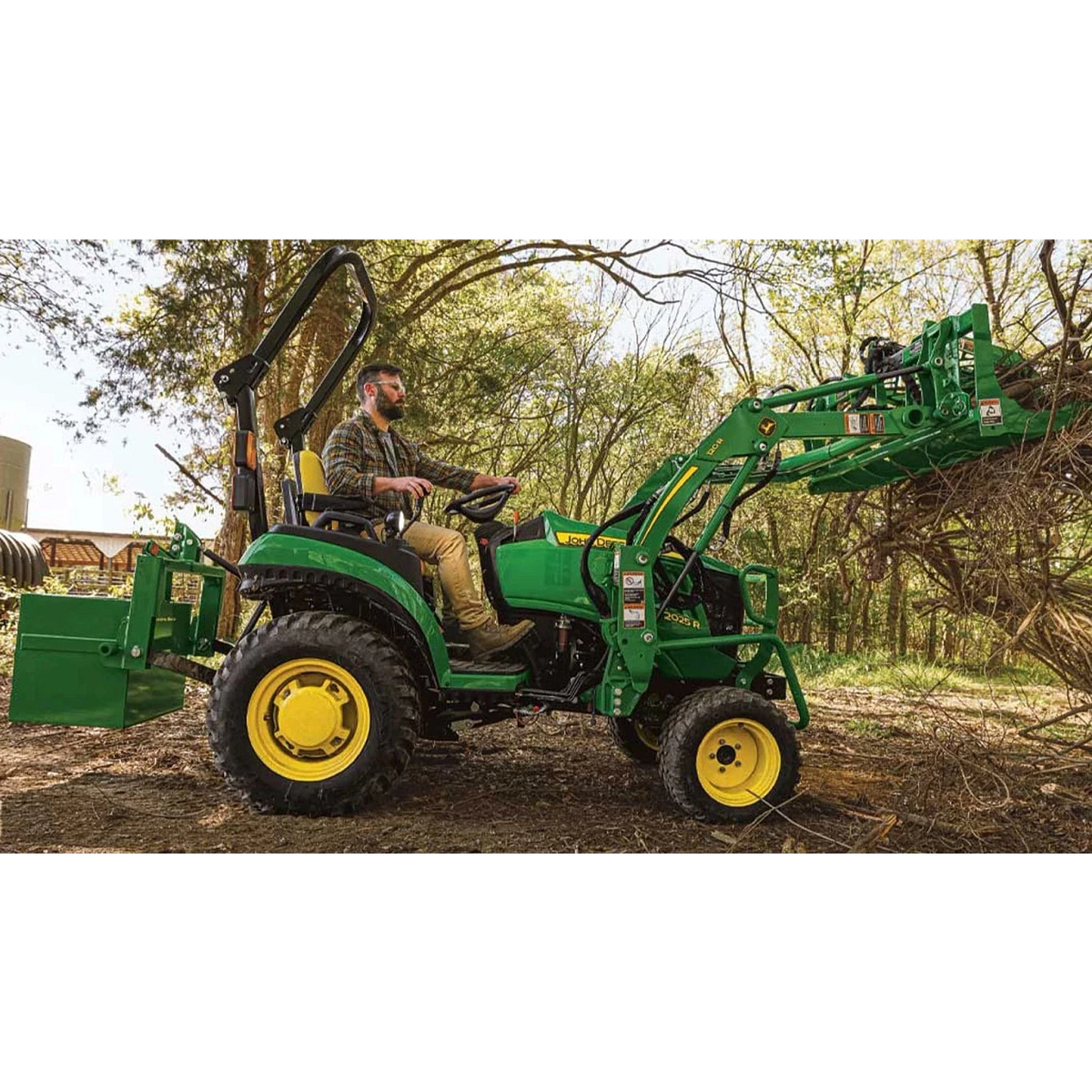 2025R Tractor 2 Series Compact Tractors with a farmer driving a tractor with a large loader behind him