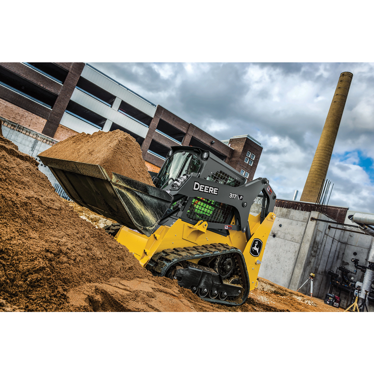 John Deere 317 compact track loader with a black front bucket, gray and yellow body, enclosed operator cab protected by metal mesh, and rubber tracks, positioned on a plain light gray background.