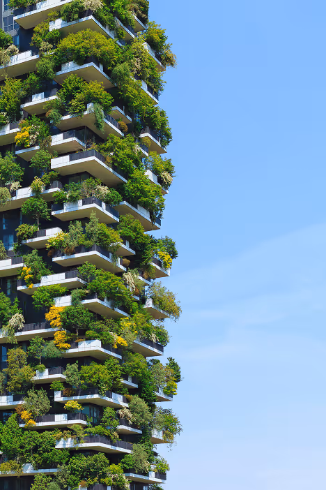 Modern residential building covered with lush green plants and trees on its balconies against a clear blue sky.
