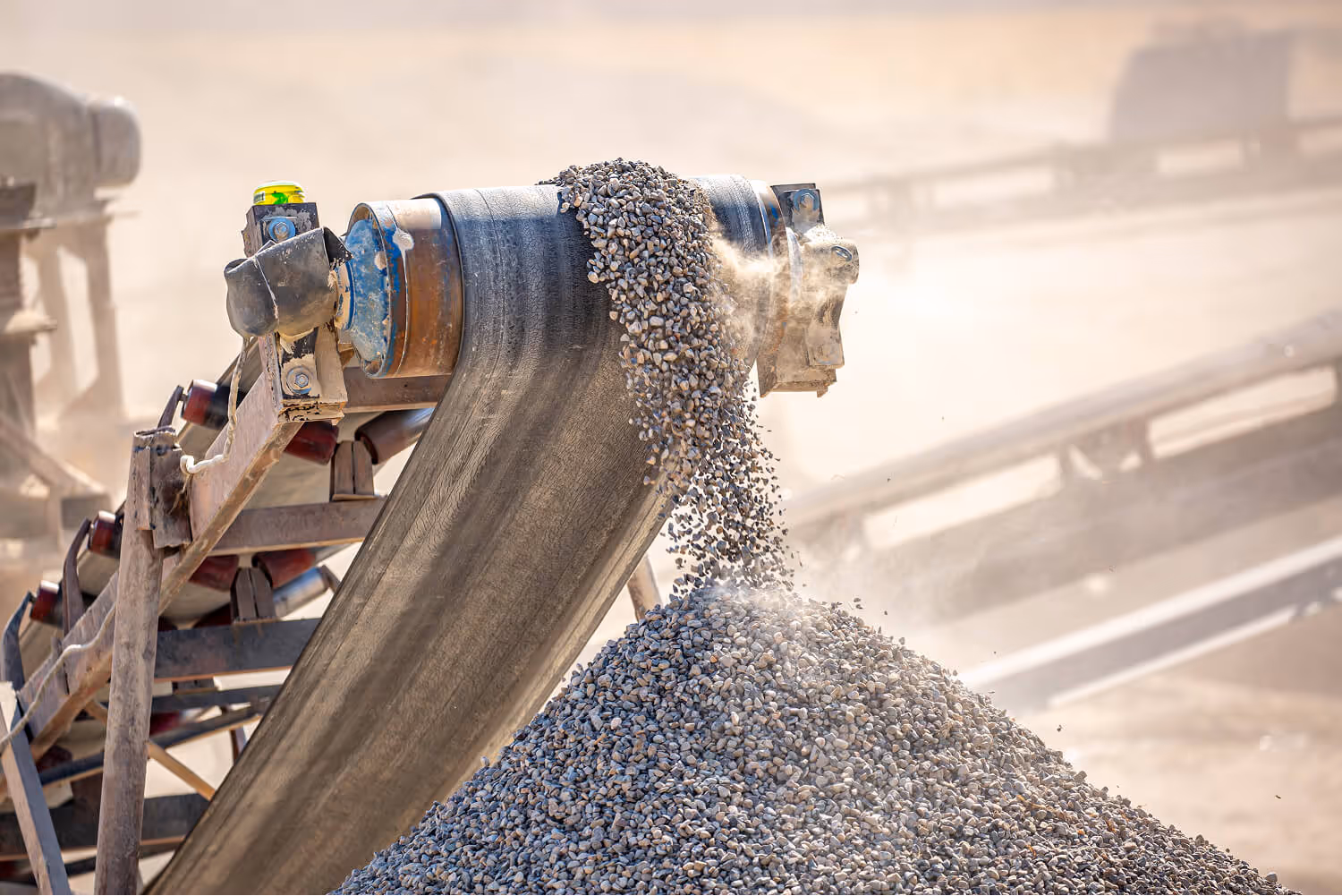 Conveyor belt depositing a pile of small gravel stones at a construction site.