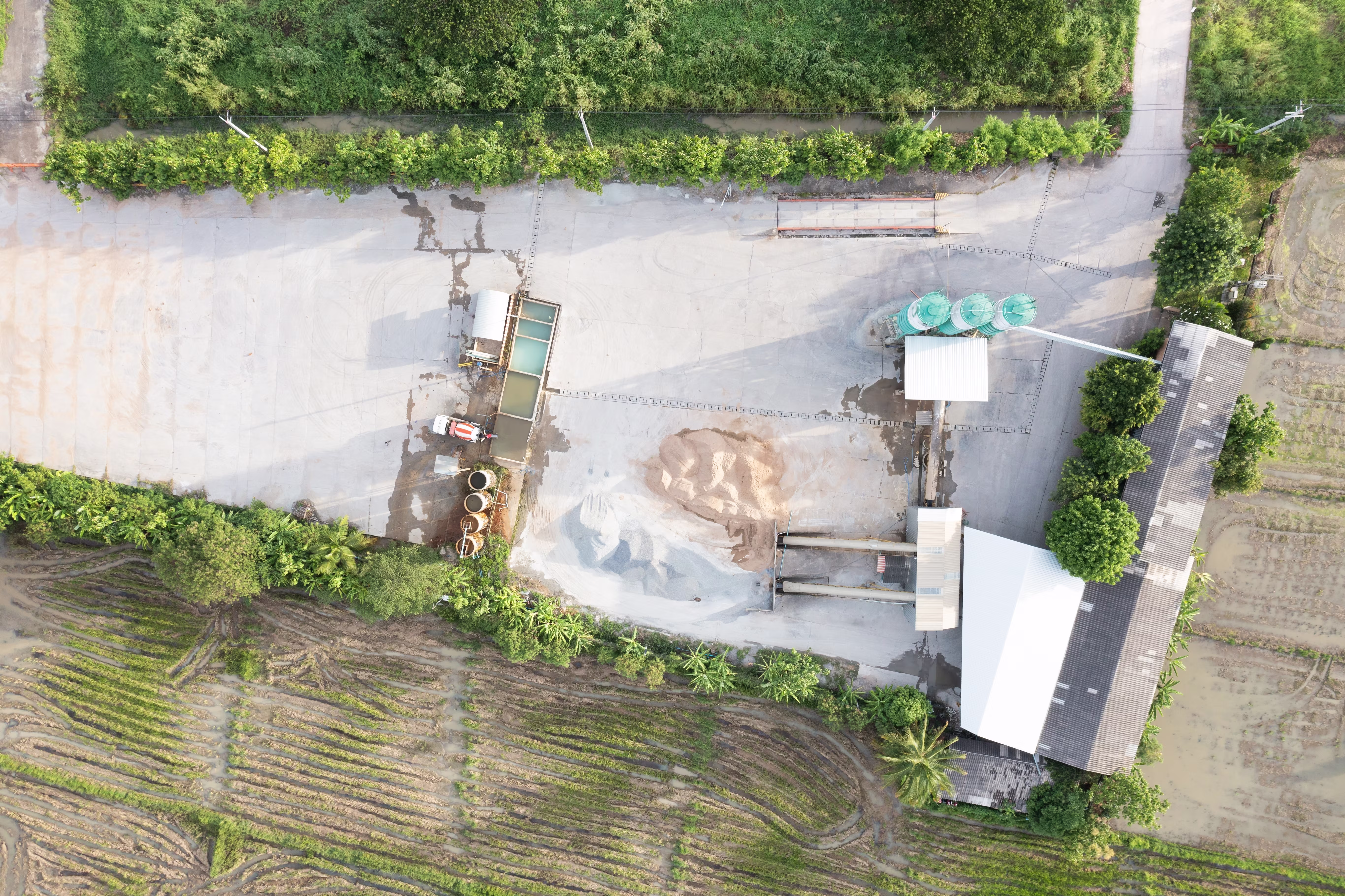 Aerial view of an industrial site with storage silos, concrete flooring, and adjacent green fields.
