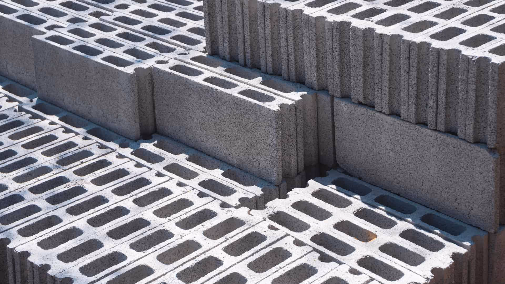 Stacked gray concrete cinder blocks arranged in rows under sunlight.