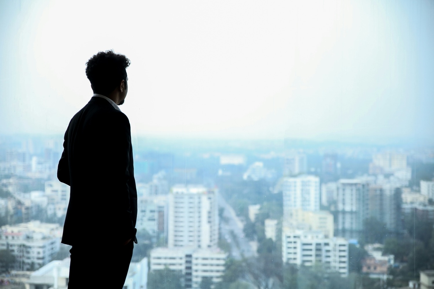 Silhouette of person in suit looking out over urban cityscape