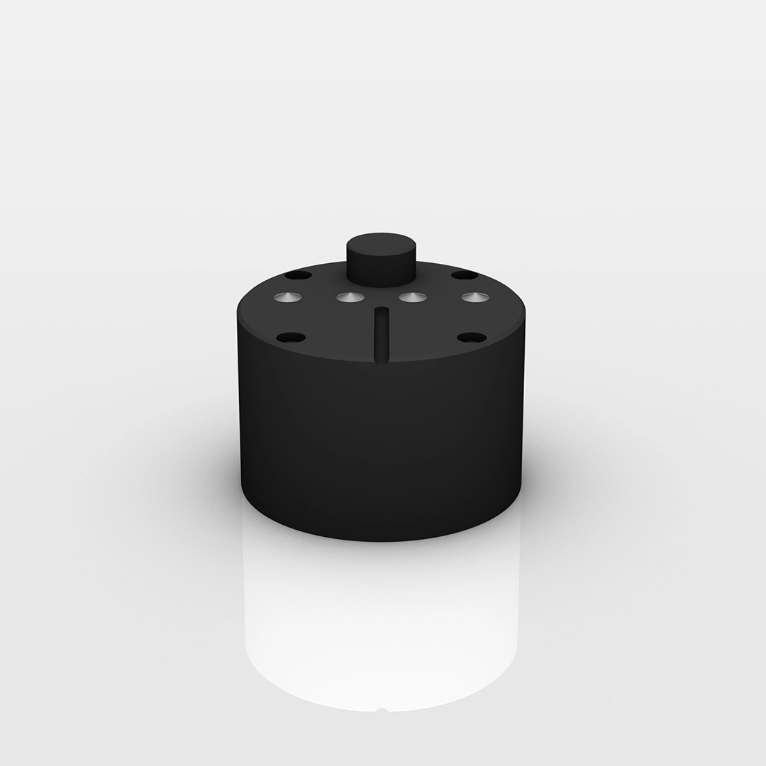 Black cylindrical object with a smaller cylinder on top and several circular holes and a vertical slit on its top surface.