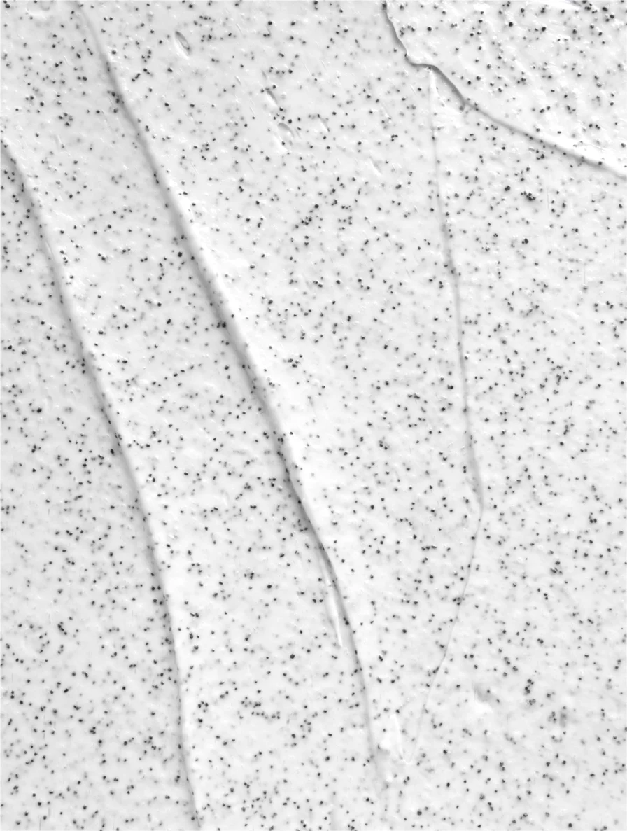Close-up of white cream or lotion with small black exfoliating particles spread across its surface.