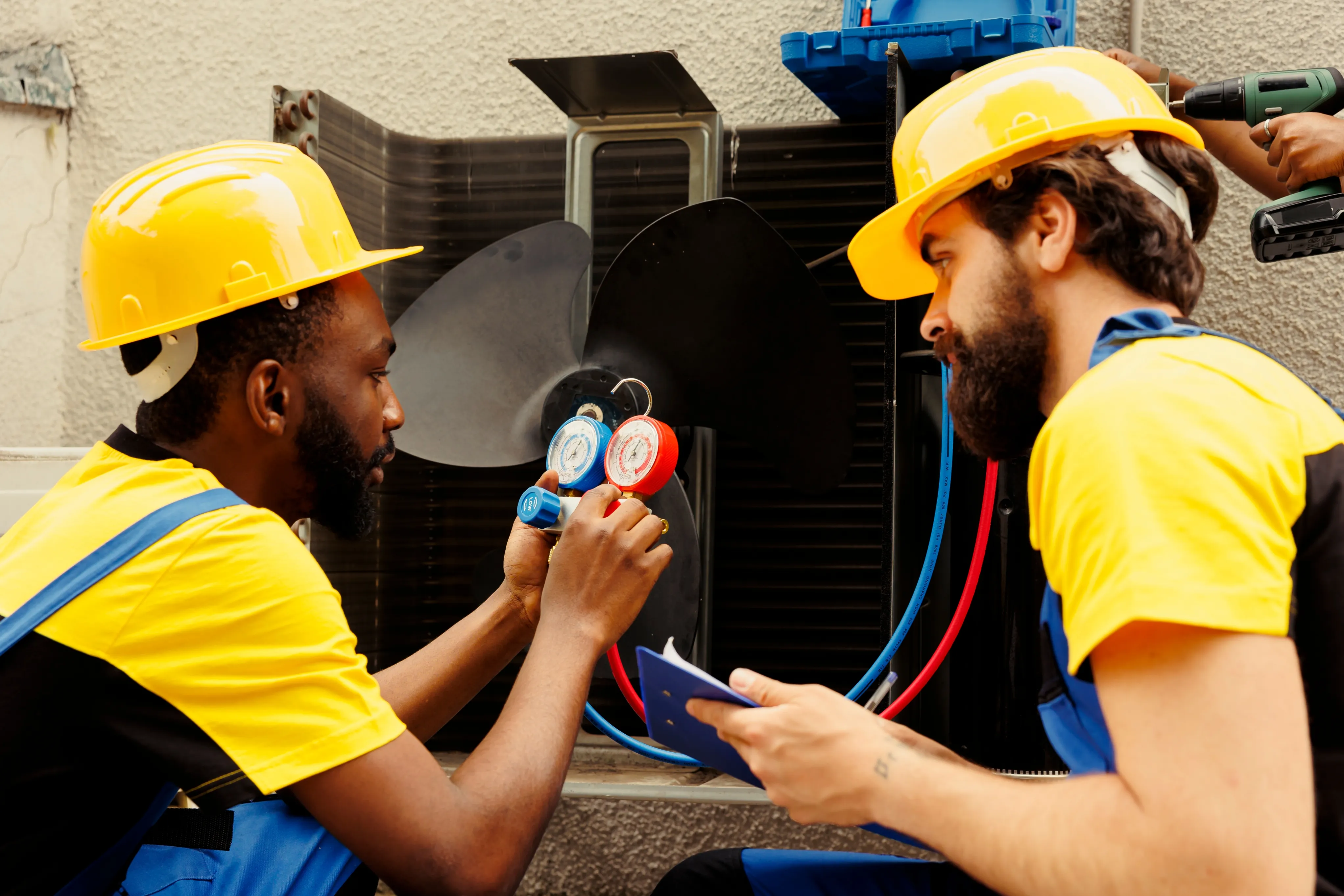 Two HVAC technicians checking refrigerant pressure on an outdoor unit