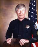 Portrait of a male police officer in uniform standing with an American flag in the background.