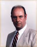 Portrait of a middle-aged man wearing a beige suit, white shirt, and striped tie with a neutral expression.