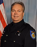 Smiling police officer in uniform standing in front of a U.S. flag.