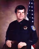 Portrait of a male law enforcement officer in uniform sitting in front of an American flag.