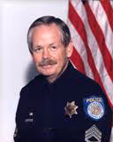 Portrait of a police officer in uniform with a mustache in front of an American flag.