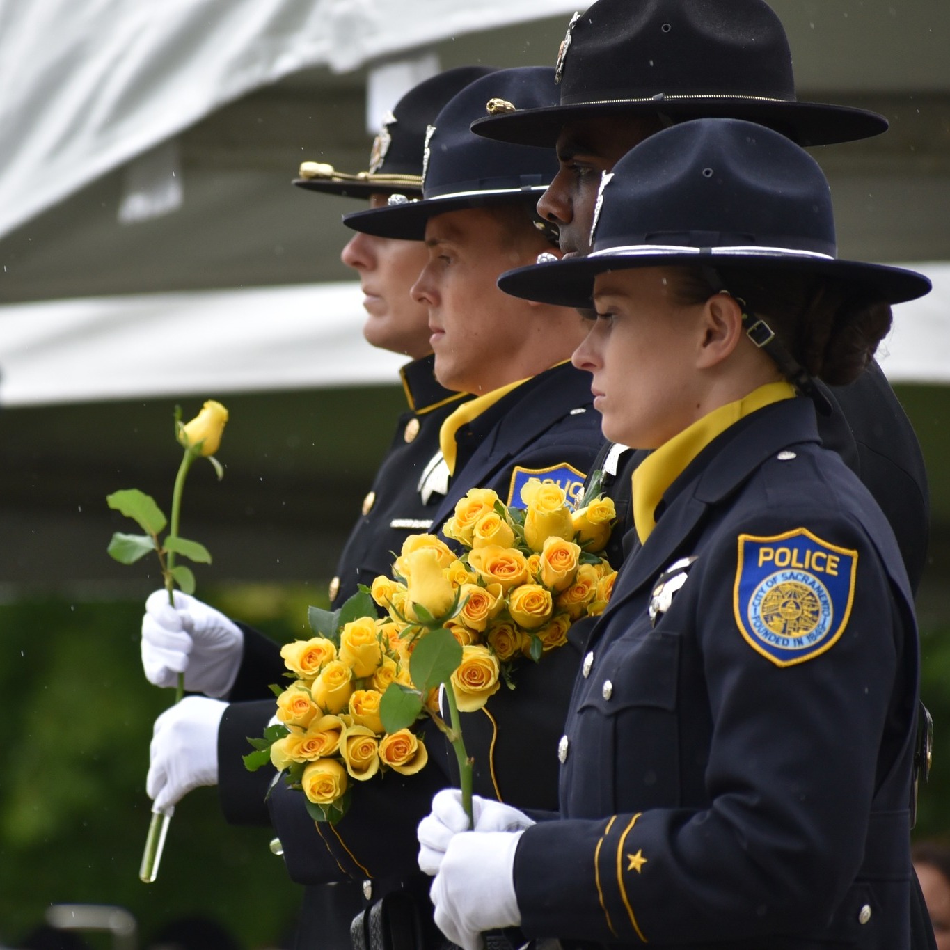 A group of seven police officers standing together in front of a banner for the Sacramento Police Officers Association. They are holding a document and wearing masks. Colorful balloons are in the background.