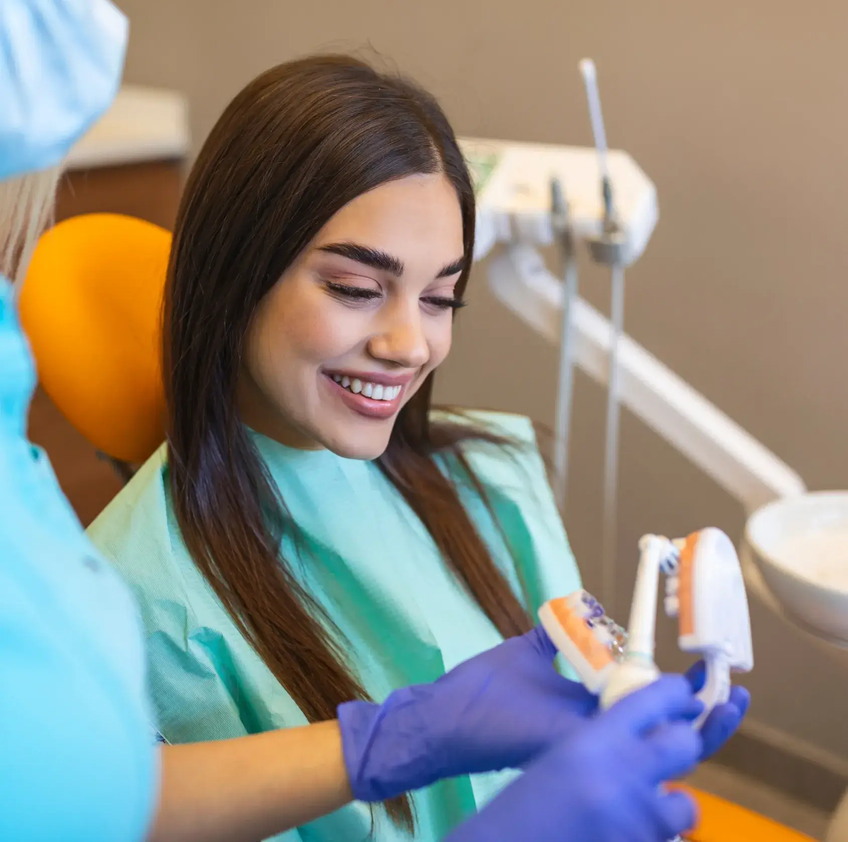 Smiling woman in dental chair looking at dental models held by a gloved dentist.