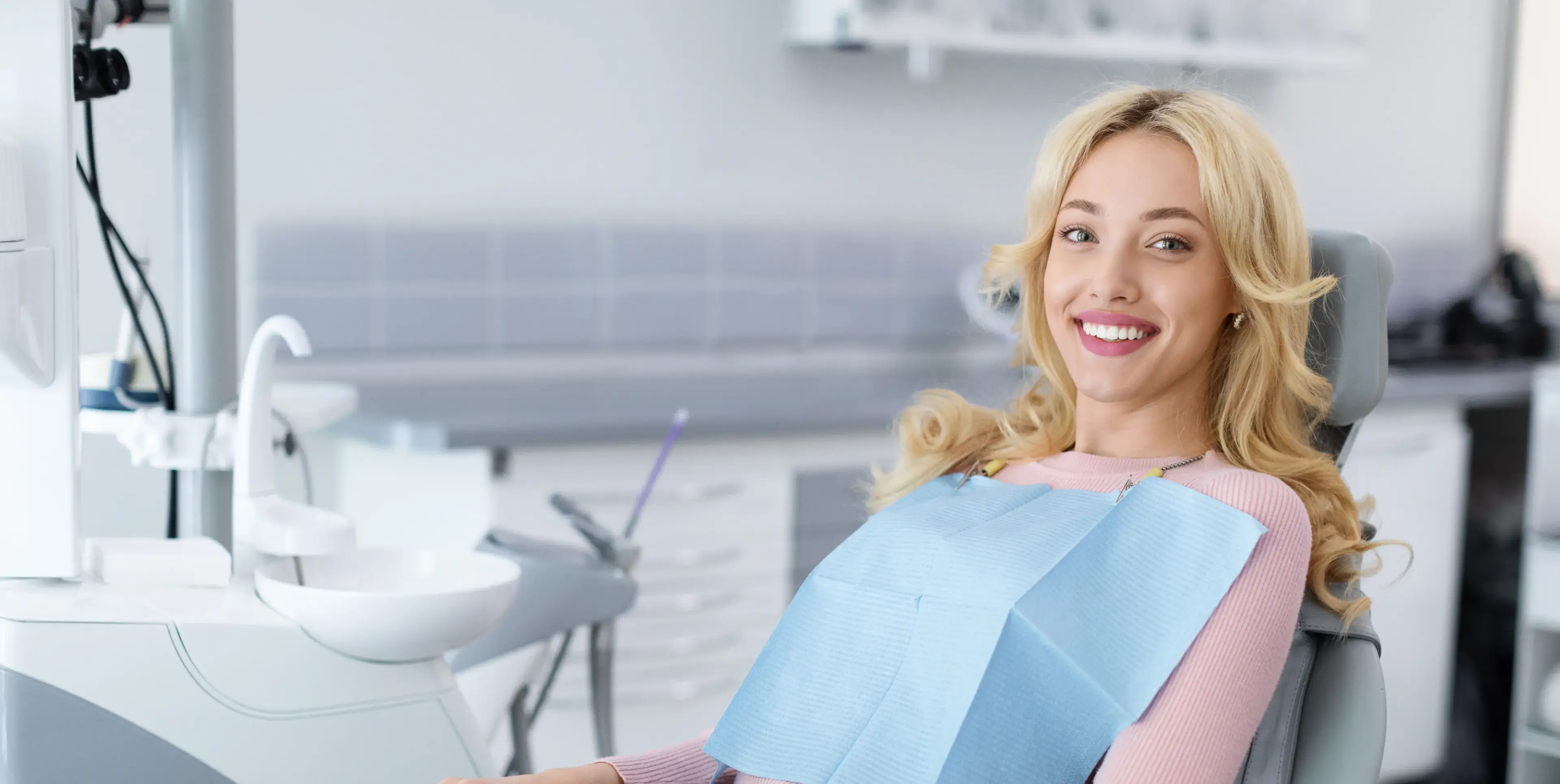 Smiling woman wearing a dental bib sitting in a dental chair in a modern clinic.