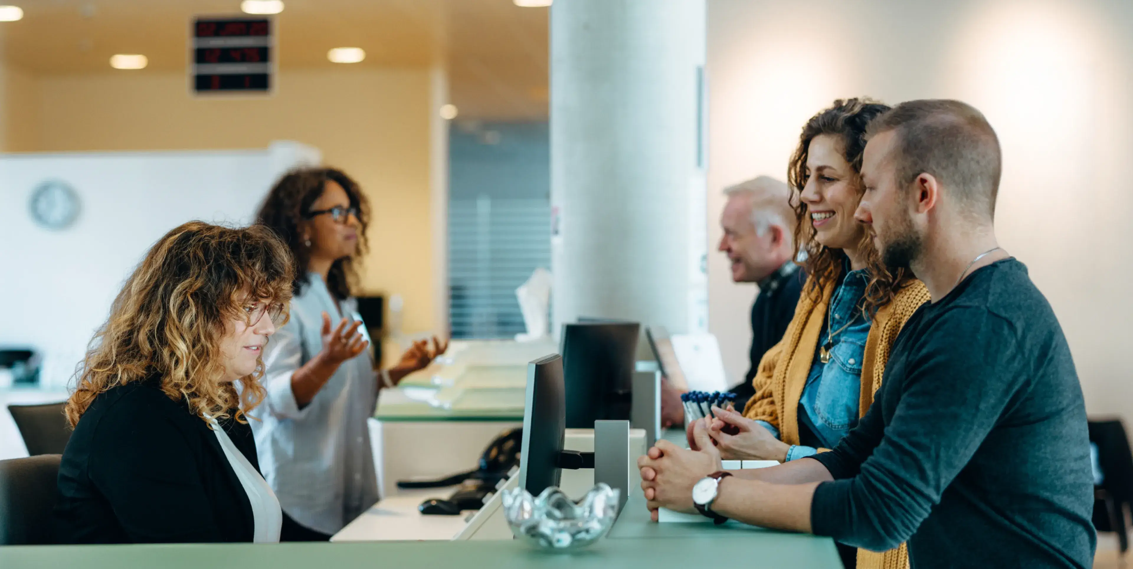 Two women and a man speaking with reception staff at an office counter.
