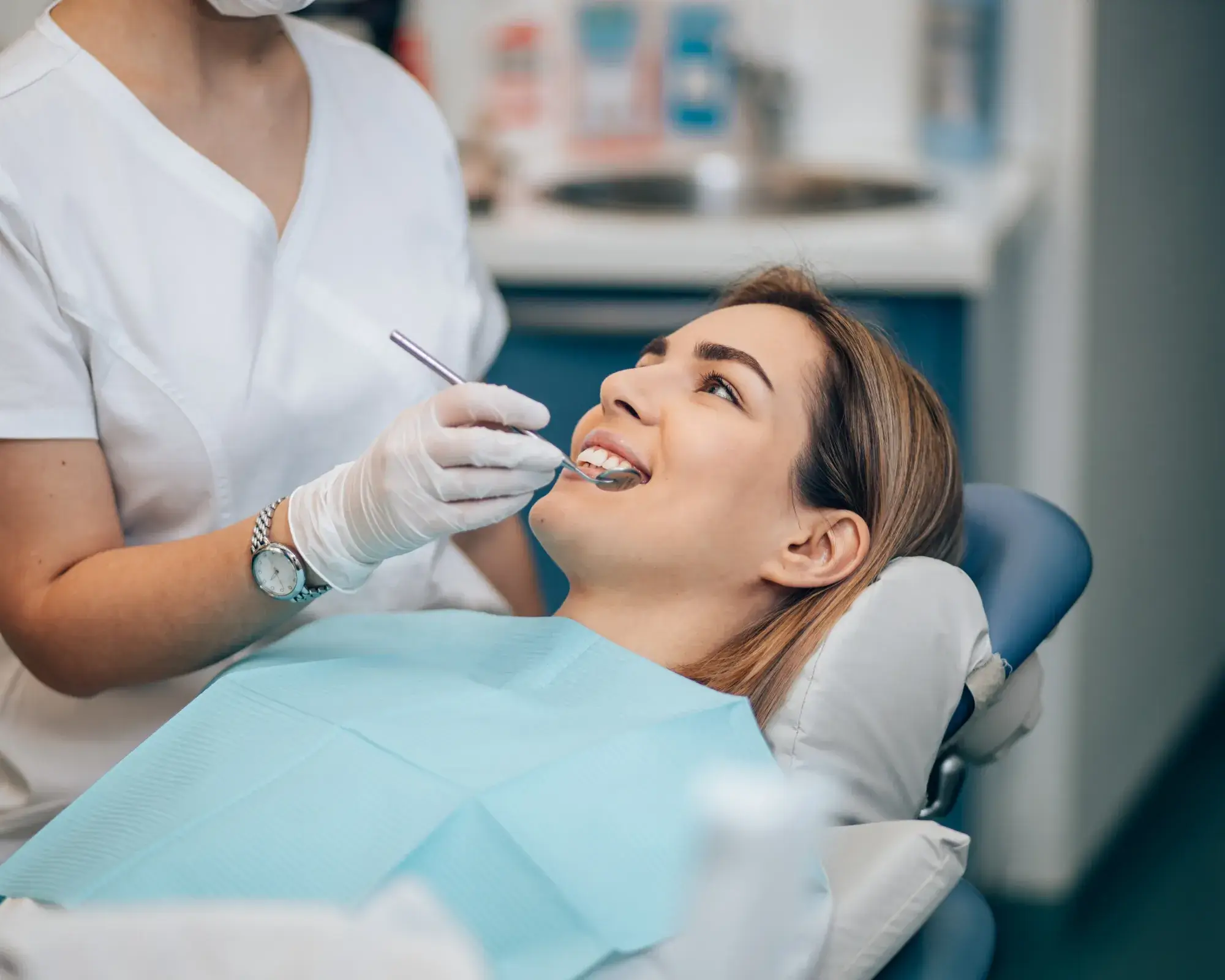Dentist wearing gloves using dental mirror to examine smiling woman's teeth in a dental clinic.