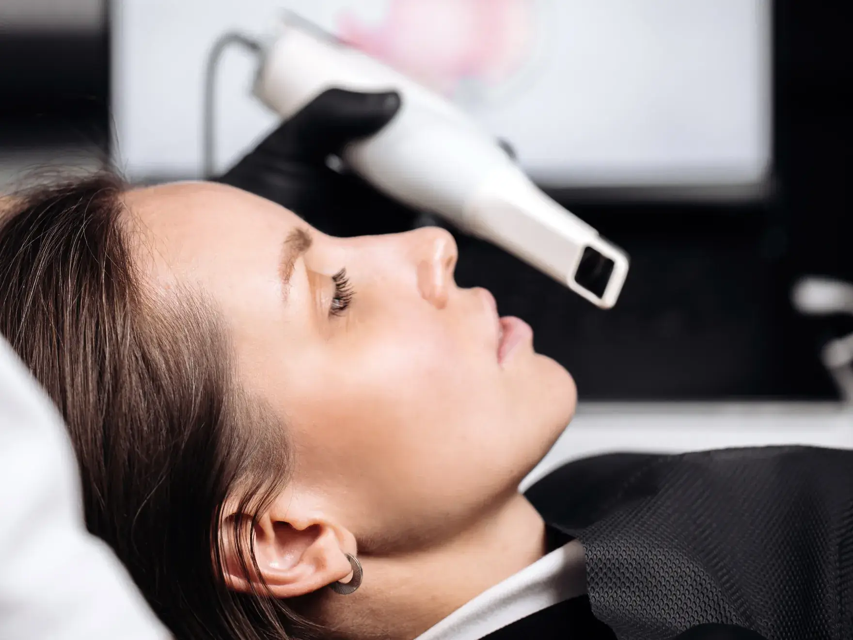 Woman receiving a non-invasive facial treatment with a handheld device operated by a gloved technician.