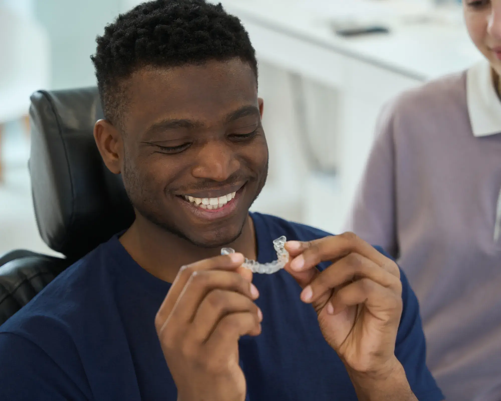 Smiling man holding a clear dental aligner in his hands, sitting in a dental office.