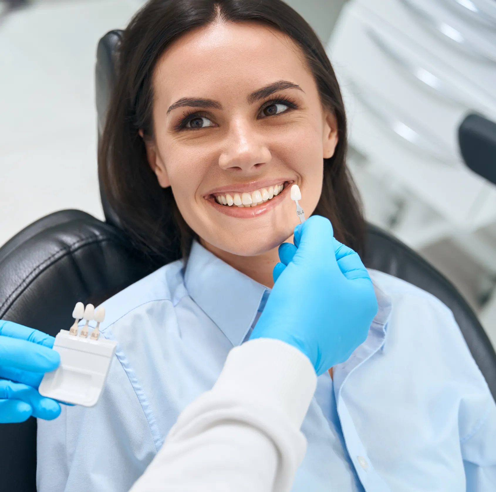 Dentist holds dental veneer shades up to a smiling woman's teeth for color matching.