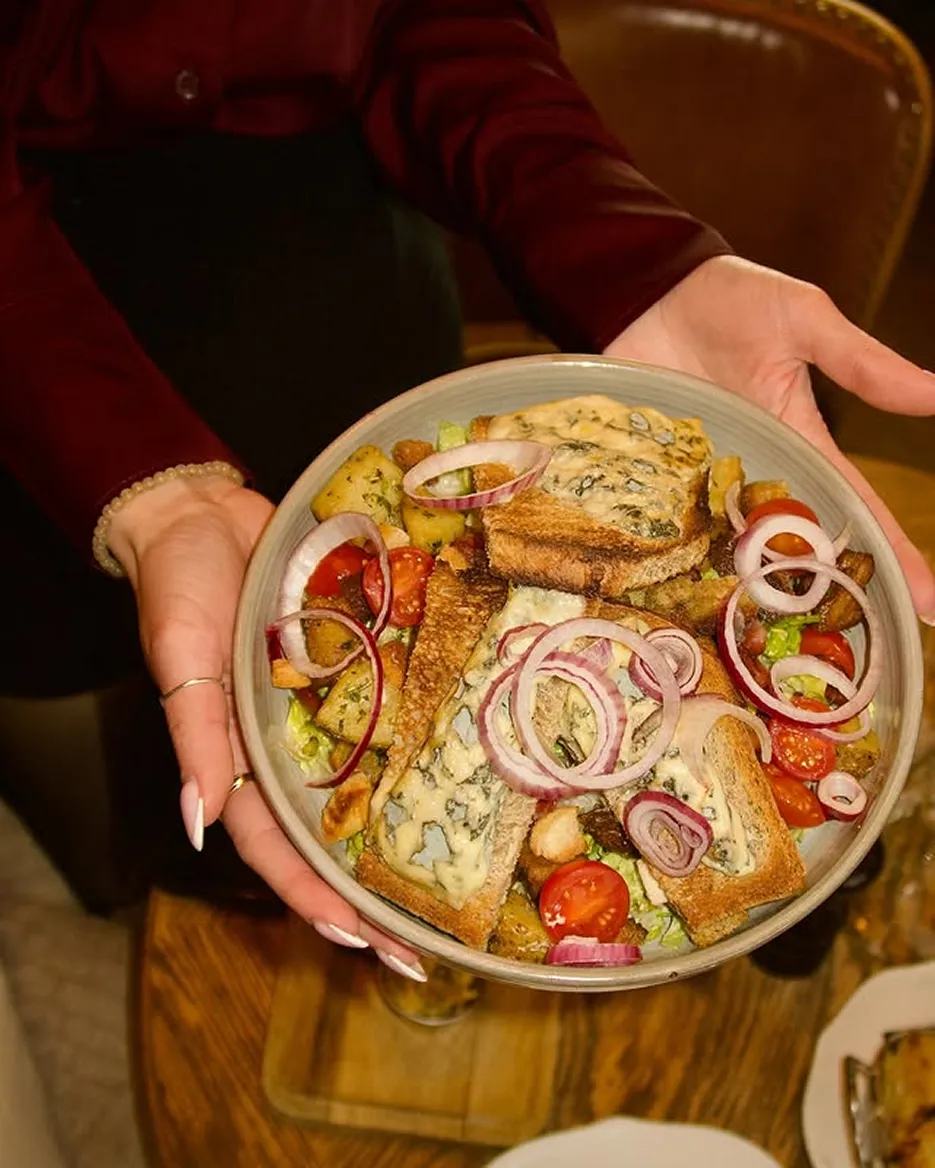 Hands holding a bowl of salad with cherry tomatoes, toasted bread with blue cheese, red onion rings, and croutons.