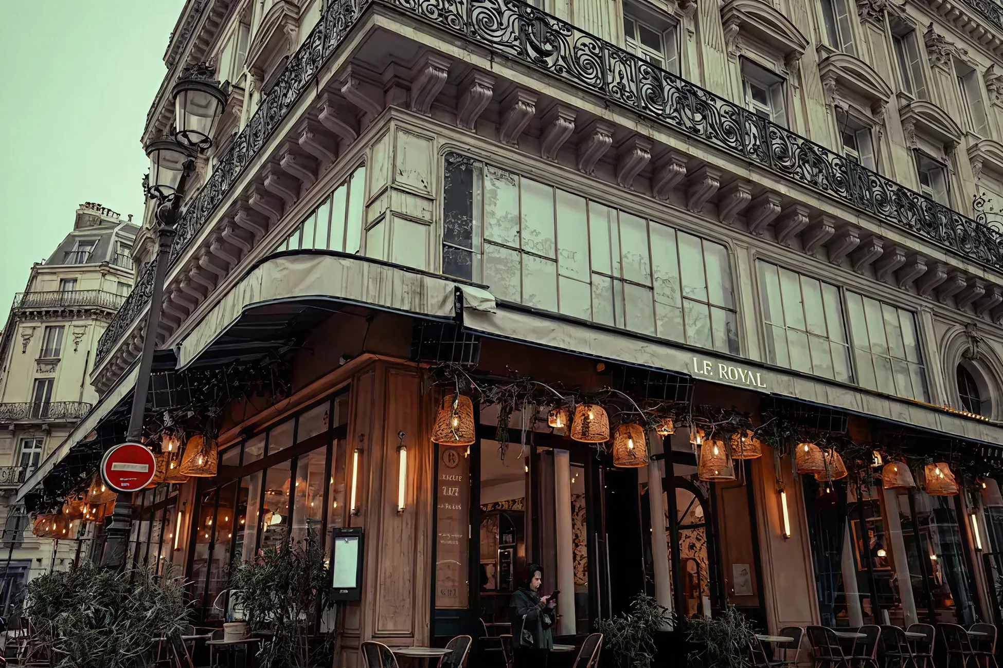Corner view of Le Royal café with warm hanging lights, outdoor seating, and a person standing by the entrance.