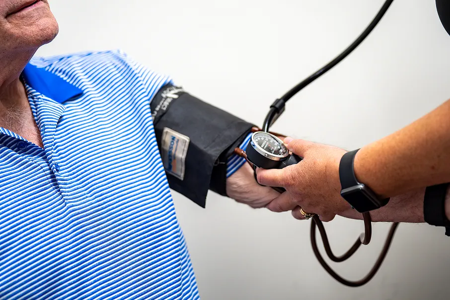 Healthcare professional measuring blood pressure of a man in a blue striped shirt using a sphygmomanometer.