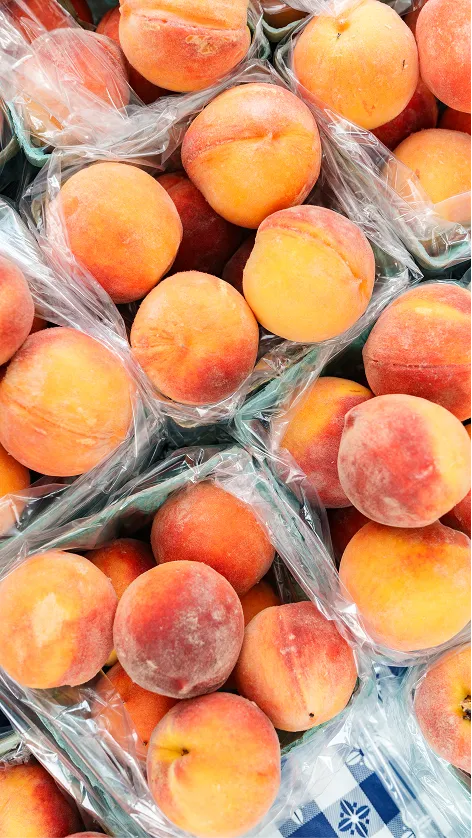 Several clusters of fresh peaches packed in plastic-lined green containers on a market table.