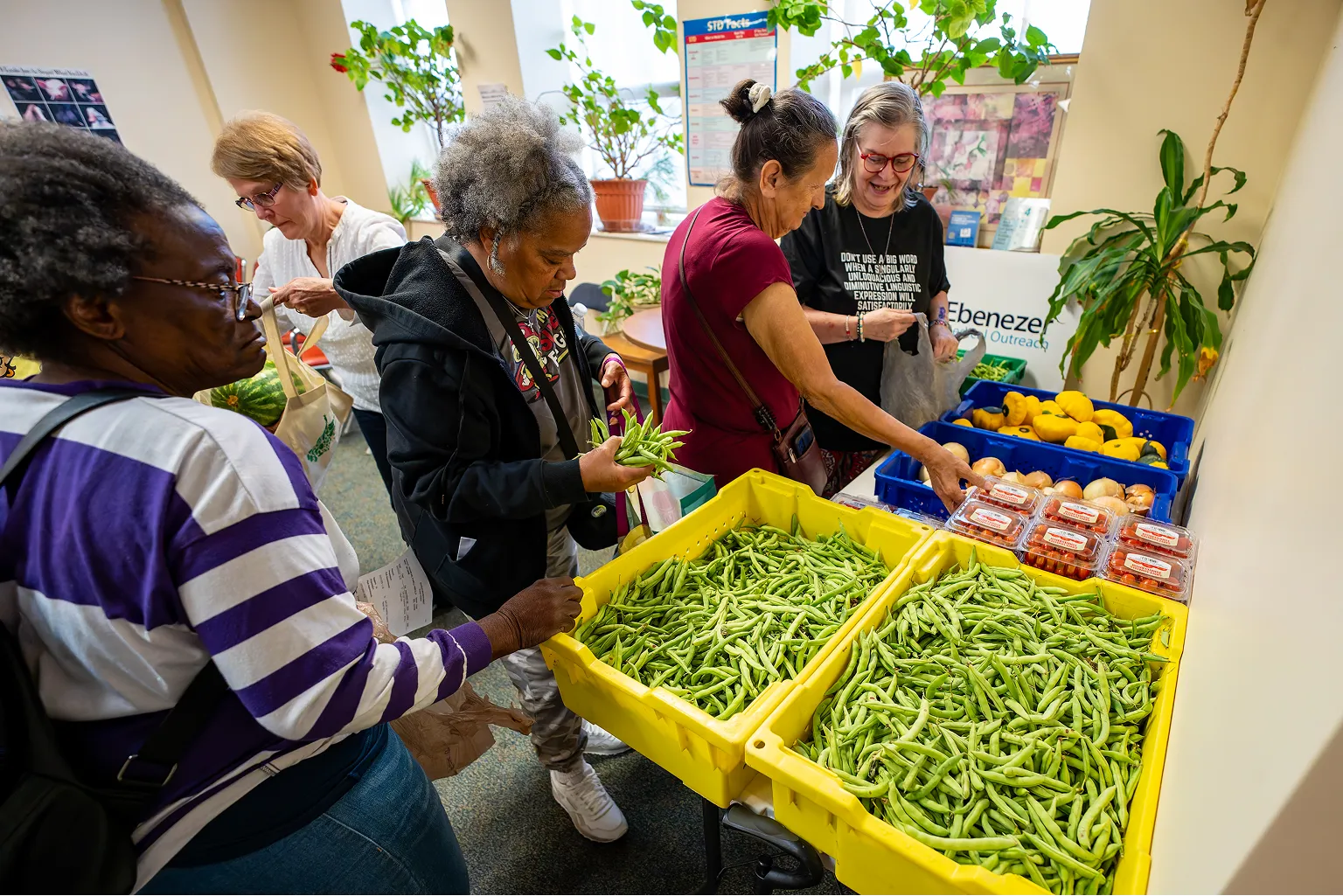 People selecting fresh green beans and other vegetables at an indoor food distribution table.